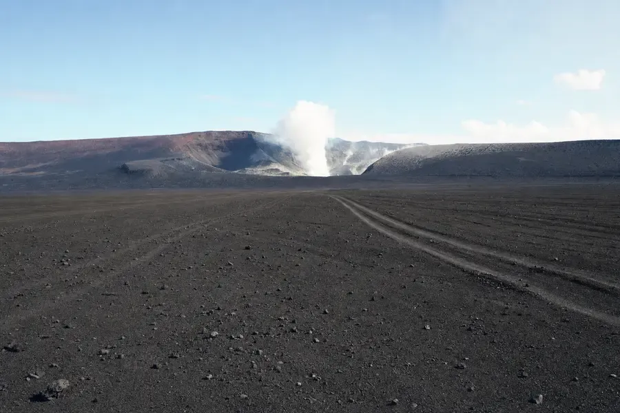 A black volcanic ash plain running to a distant crater rim venting steam (AI-generated image)