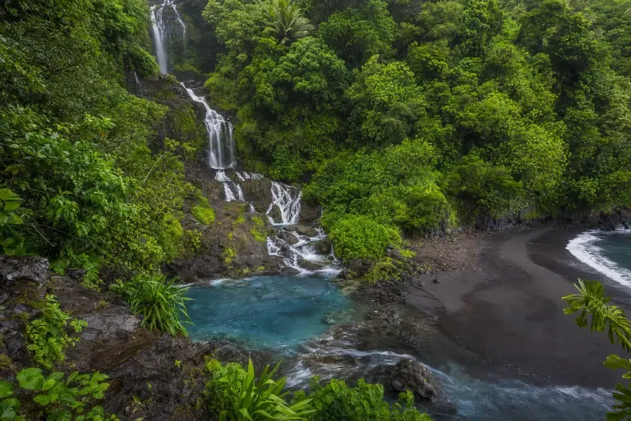 A tall waterfall dropping through rainforest into clear pools near the shore (AI-generated image)