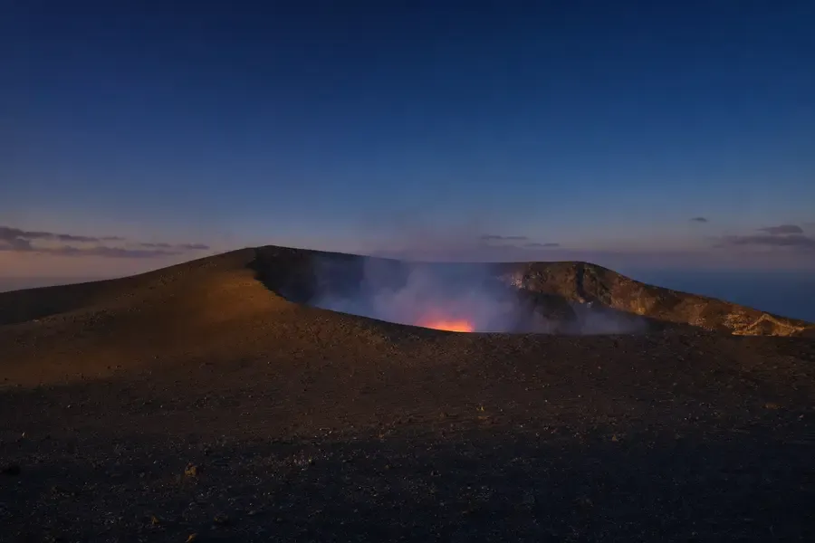 Mount Yasur at dusk, ash plain in the foreground and a glow inside the crater (AI-generated image)